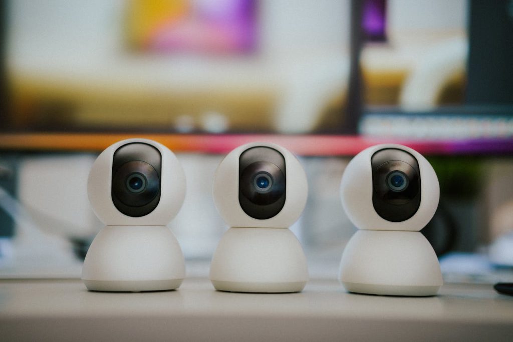 pexels photo 28117882 Three modern smart home security cameras placed on a table indoors with a blurry background.